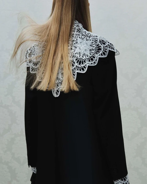 Blonde woman's back, wearing black dress with large white lace collar, against neutral background. Fashion photography. 