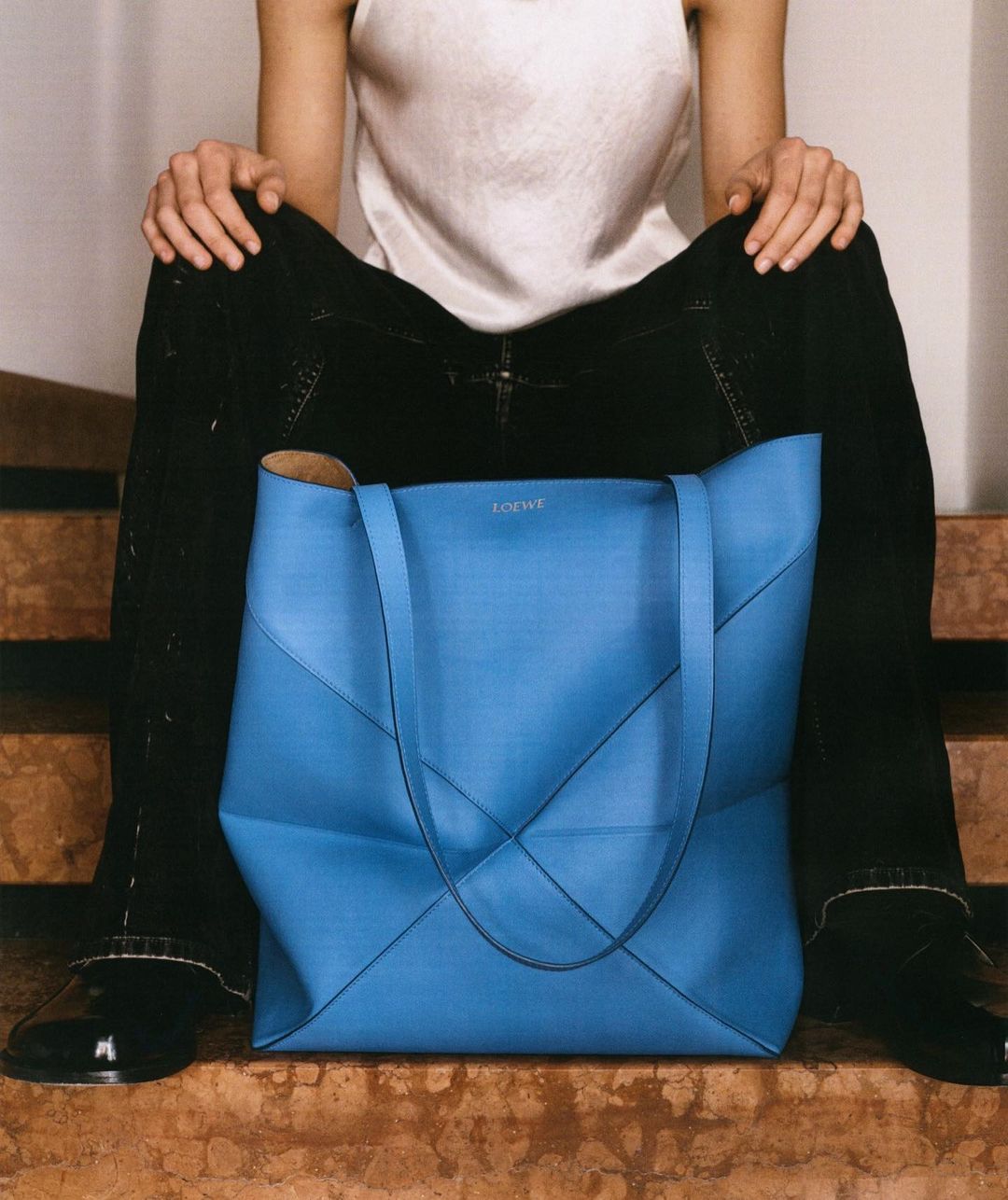 Adult female sits with a light blue leather handbag on marble steps in an eye-level medium shot, showcasing fashion and casual style.