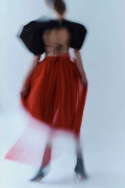 Blurred fashion shot of a woman in a red skirt and black top. The woman is facing away from the camera in a studio setting.