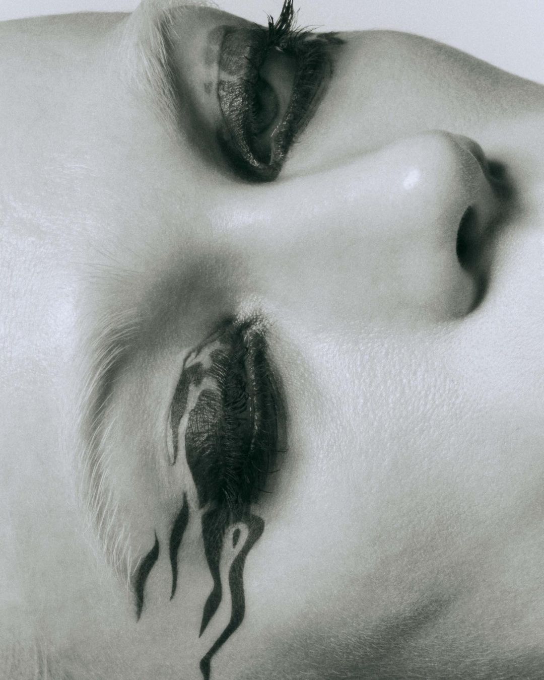 Monochromatic close-up shot featuring a woman's face with artistic makeup forming a dripping paint or tattoo effect under her eye.