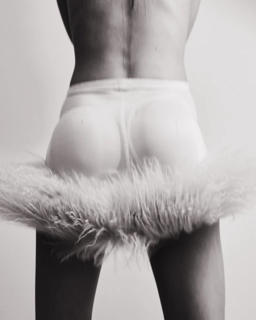 Back view of a person in a skirt with fur trim, captured in a black and white photo with a seamless white backdrop in a photo studio.
