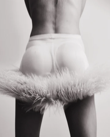 Back view of a person in a skirt with fur trim, captured in a black and white photo with a seamless white backdrop in a photo studio.