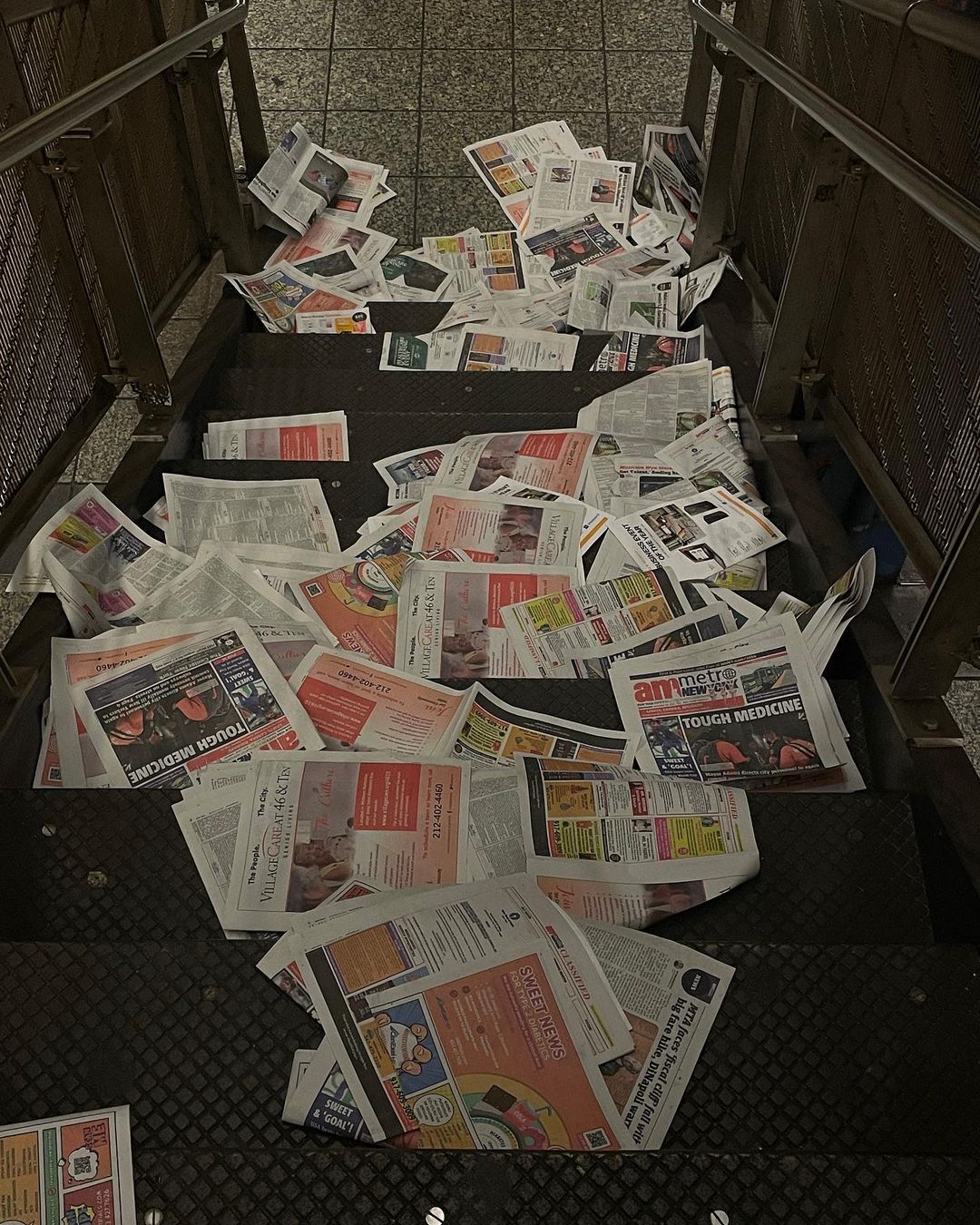 View of newspapers scattered all over the stairs, indicating potential distribution or leftover papers in a public transit setting.