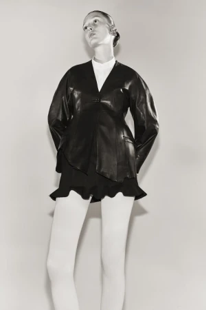 Model in black leather jacket and white tights against a plain light background photographed by Sarah Blais