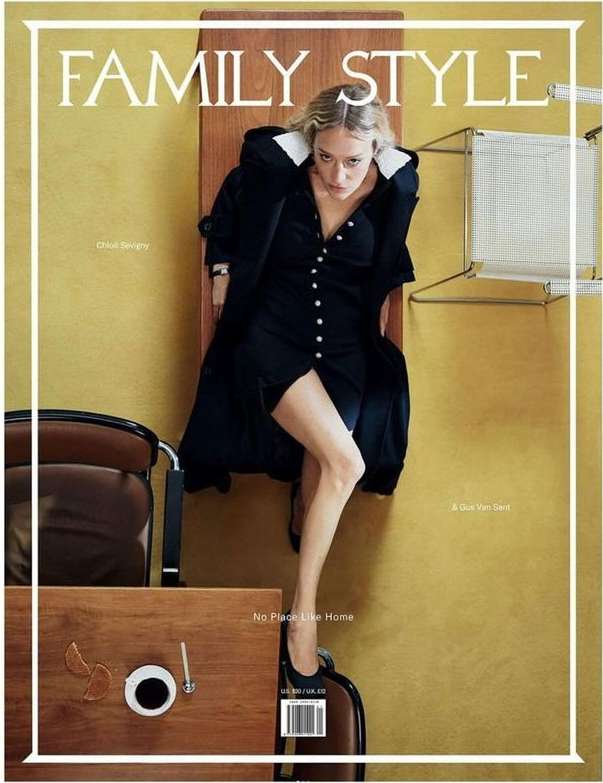 Fashion magazine cover with a woman in a black dress and coat sitting on a wooden panel, styled with modern furniture.