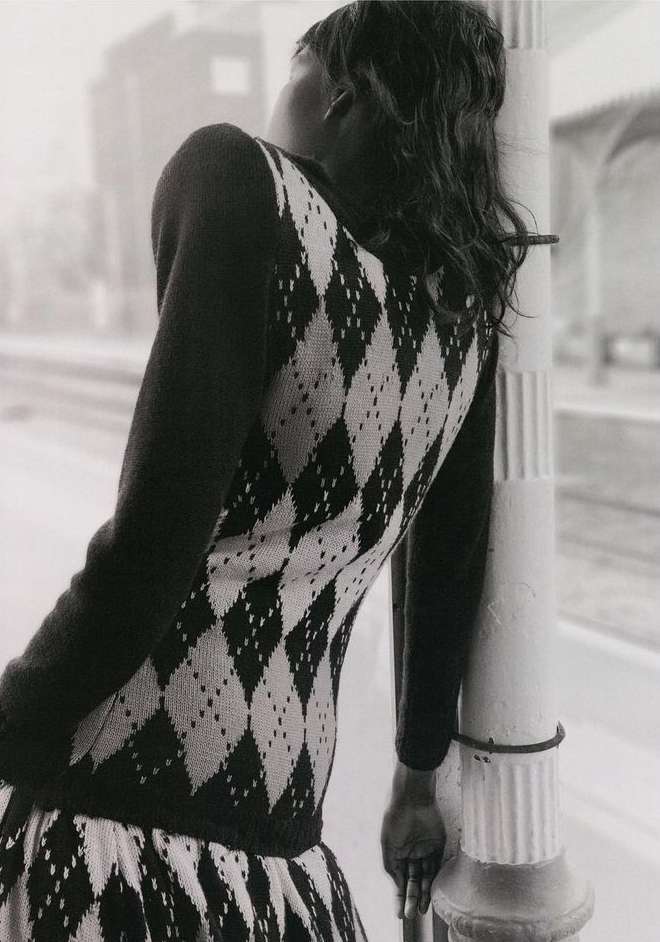 Woman with black hair and a patterned dress leans against a pole, creating a fashion forward, black and white editorial style shot.