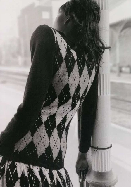 Woman with black hair and a patterned dress leans against a pole, creating a fashion forward, black and white editorial style shot.
