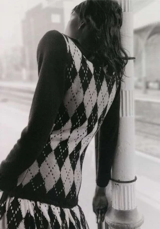 Woman with black hair and a patterned dress leans against a pole, creating a fashion forward, black and white editorial style shot.