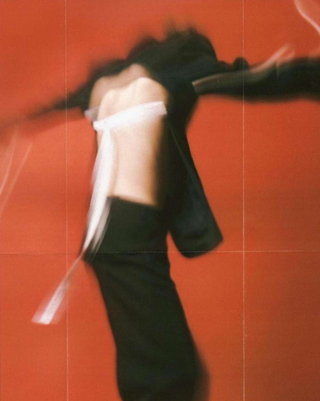 Abstract fashion photography featuring a person in motion with a blurred effect on a red background, creating a dynamic and artistic visual.
