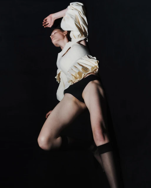 Low-angle shot of a solo female model in a light top and black bottoms striking a pose against a dark backdrop in a studio setting.