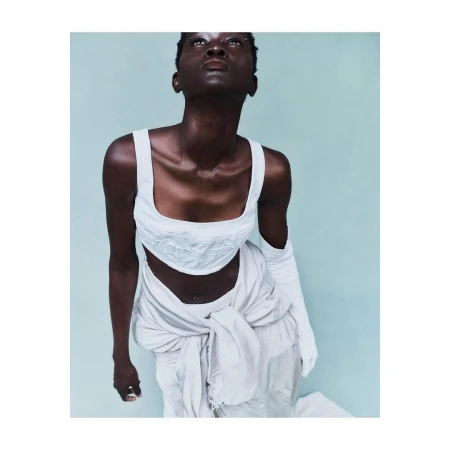 African-American female fashion model poses in studio with off-white crop top, skirt tied at waist, long gloves, and upward gaze.
