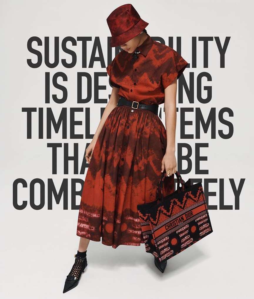 A woman in a red patterned dress and matching bucket hat, holding a branded tote, poses against a backdrop of bold white text.