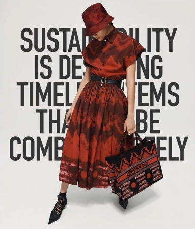 A woman in a red patterned dress and matching bucket hat, holding a branded tote, poses against a backdrop of bold white text.