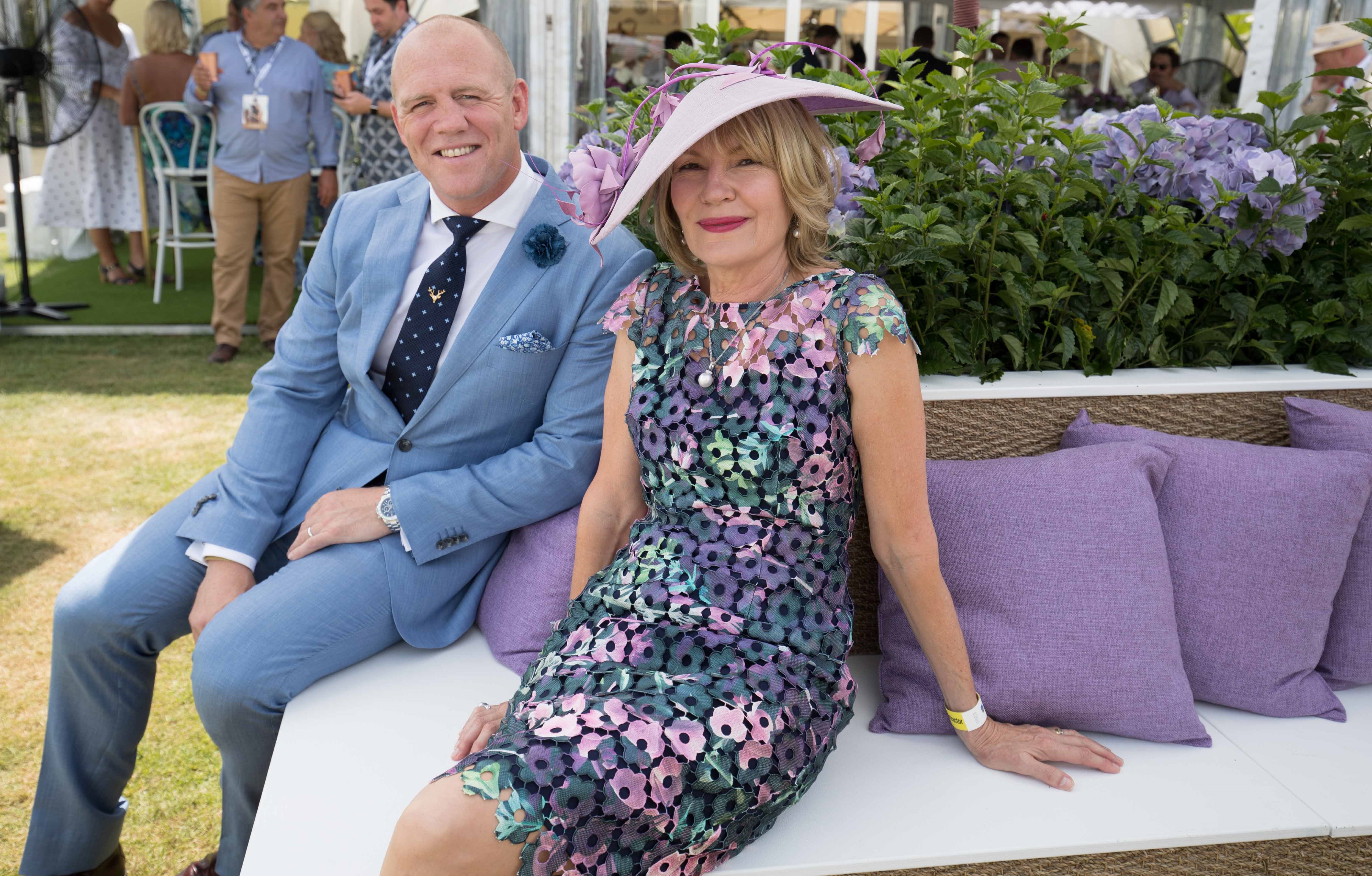 A man in a light blue suit and a woman in a floral dress and pink hat seated together outdoors.