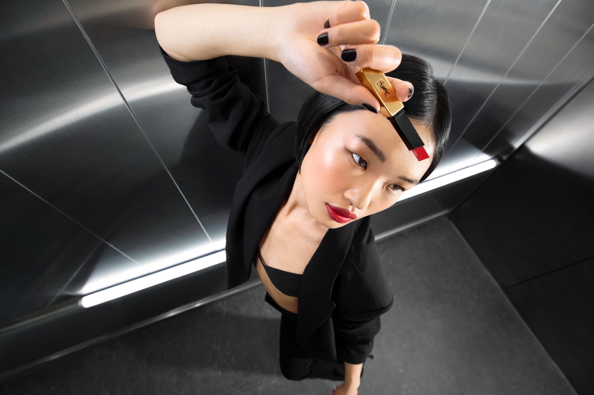 Glamorous Asian woman poses in a modern setting, showcasing red lipstick. The shot features a low angle and red lipstick.