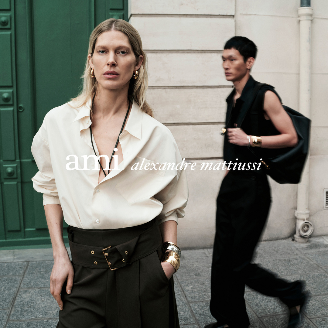 Editorial fashion shoot featuring a blonde model in a white shirt and wide-leg pants, and a man in black sleeveless top and trousers.