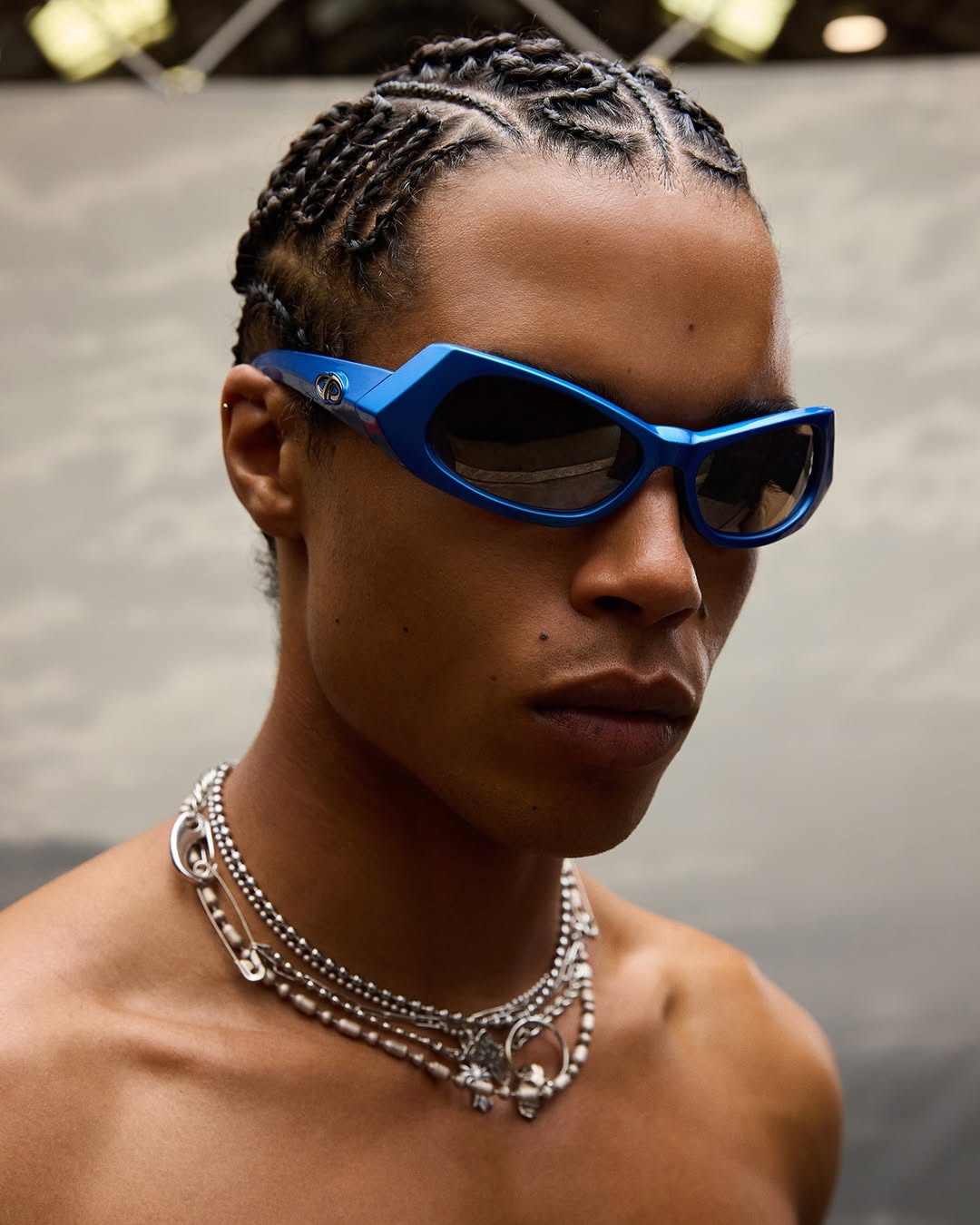 Close-up of a man wearing blue sunglasses and silver necklaces, presenting a fashion-forward and stylish look.