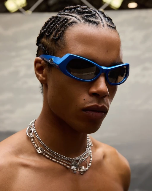 Close-up of a man wearing blue sunglasses and silver necklaces, presenting a fashion-forward and stylish look.
