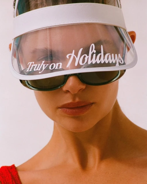 Close-up shot of a woman wearing a white visor and sunglasses with the text 'Truly on Holidays' visible on the visor lens.