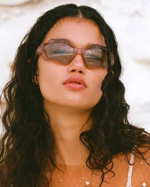 Close-up of an adult female wearing decorative sunglasses, posing indoors with a neutral facial expression and dark wavy hair.