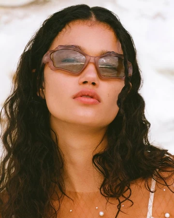 Close-up of an adult female wearing decorative sunglasses, posing indoors with a neutral facial expression and dark wavy hair.