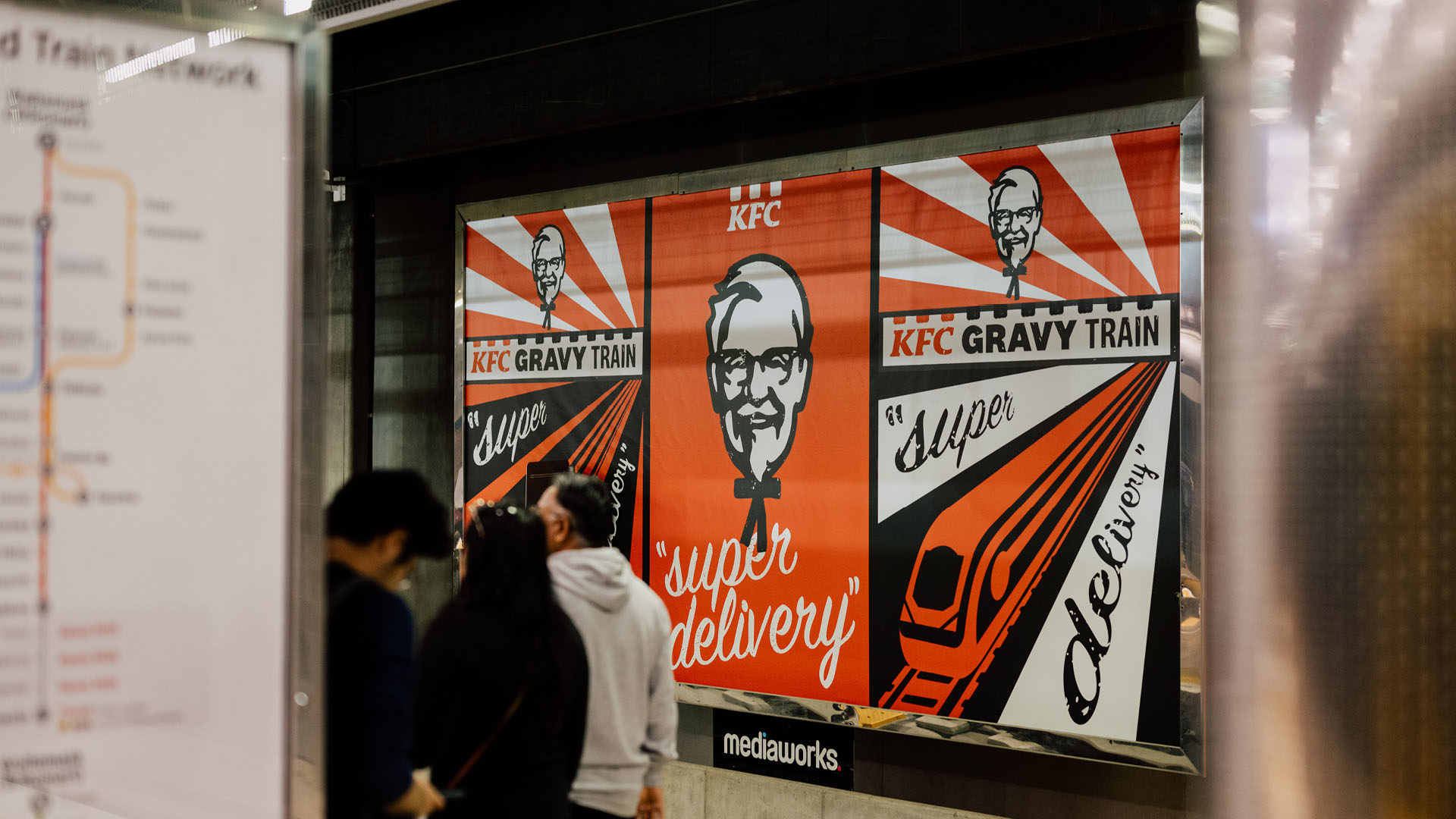 KFC advertisement in a subway station featuring Colonel Sanders, 'Gravy Train' text, and an image of a train for food delivery service.