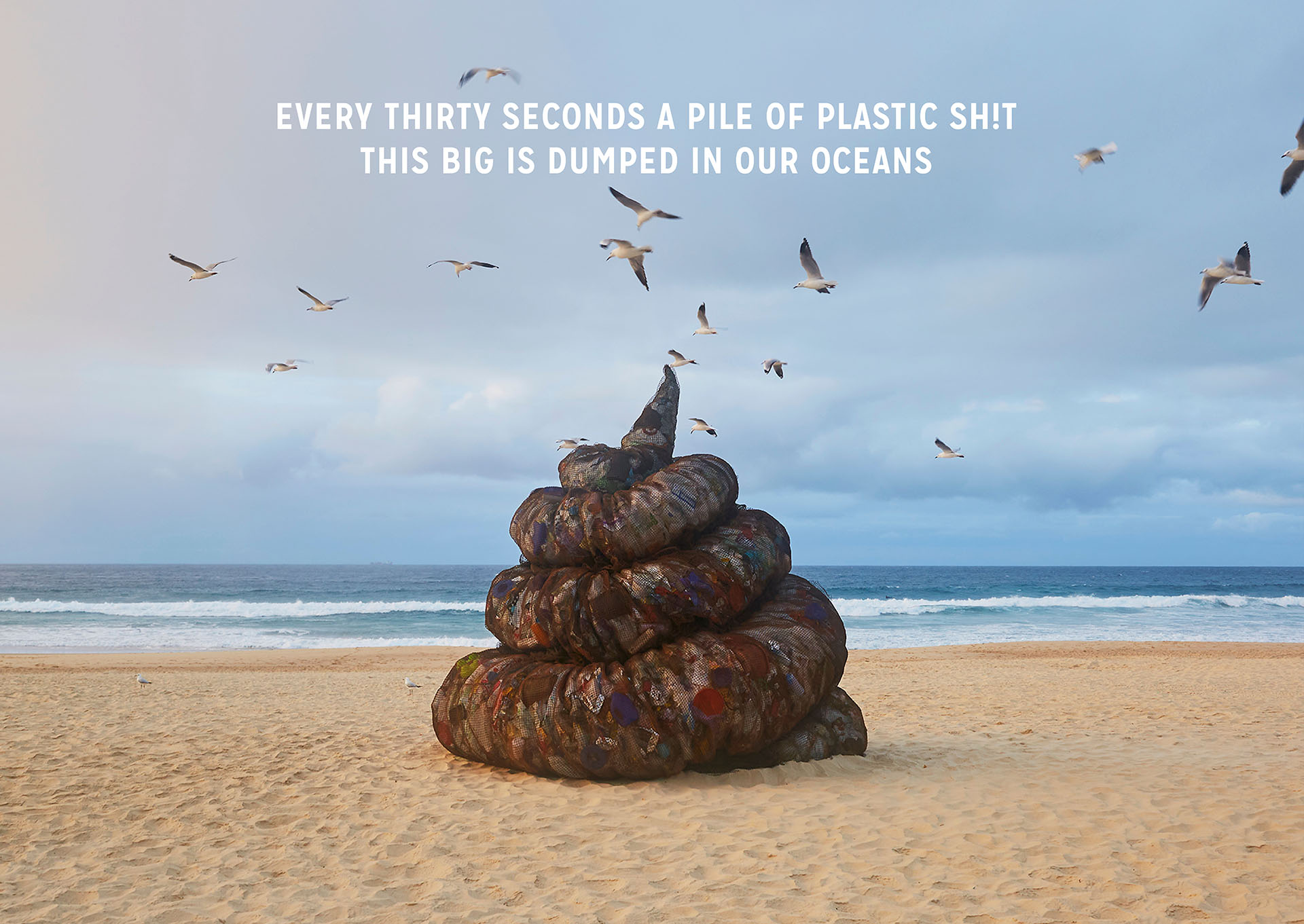 A pile of simulated trash sits on a beach surrounded by flying seagulls; the ocean and sky are visible in the background, warning about plastic pollution.