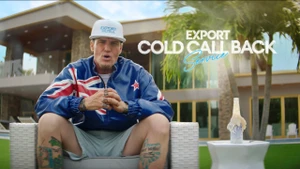 Man wearing a blue jacket with a flag design sitting outdoors in front of a modern house by Special New Zealand