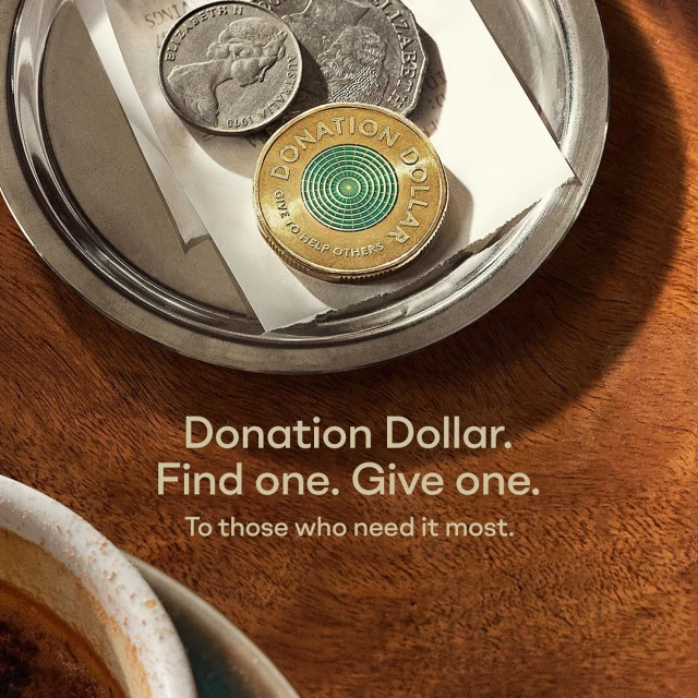 Close-up of donation dollar coin on a silver plate with other coins, set against a woodgrain background with printed text.