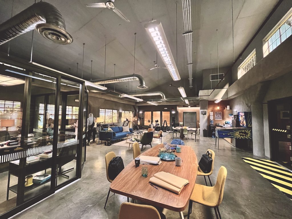 Wide shot of a brightly lit, modern office space with a large wooden conference table and chairs, with sofas and desks in the background.