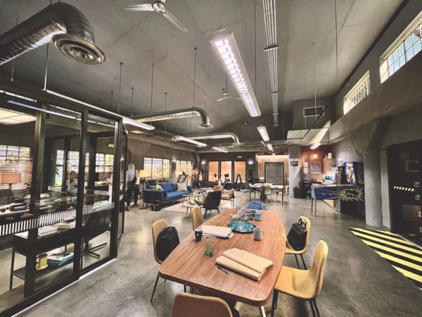 Wide shot of a brightly lit, modern office space with a large wooden conference table and chairs, with sofas and desks in the background.