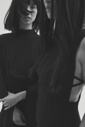 Two models in black dresses with dark hair styled by Jessica Steuart-Hoyler against a white background