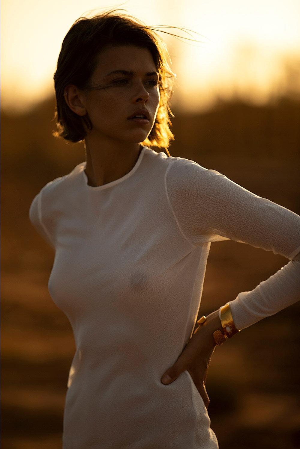 Portrait of a young woman outdoors in a long-sleeve white shirt with a serious expression, golden light, and natural setting.