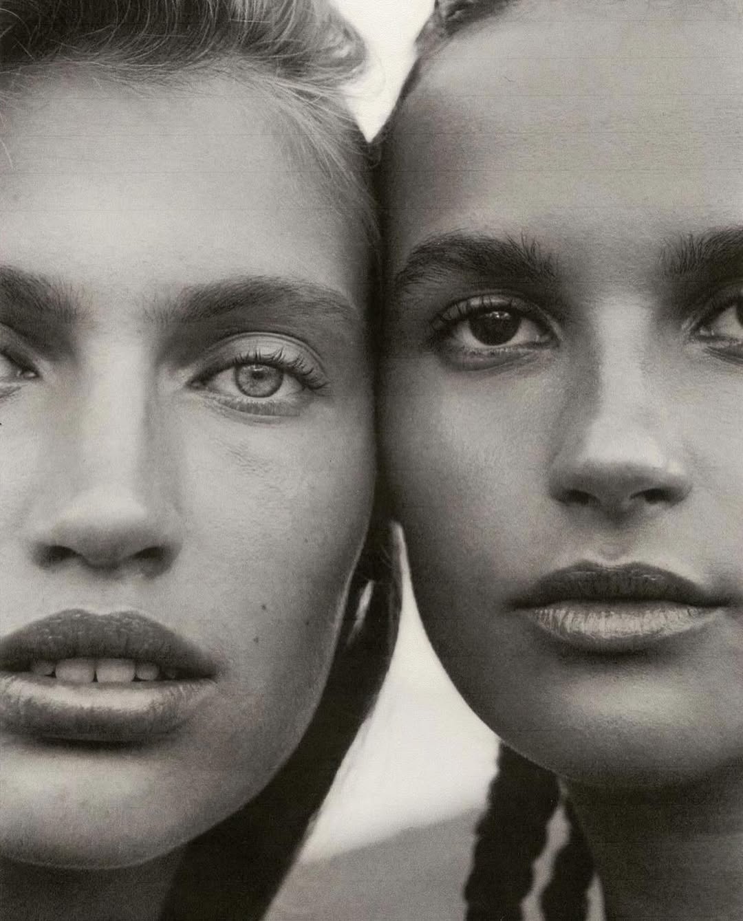 Close-up portrait of two women with contrasting skin tones and hairstyles posing together in a studio with soft, neutral lighting.