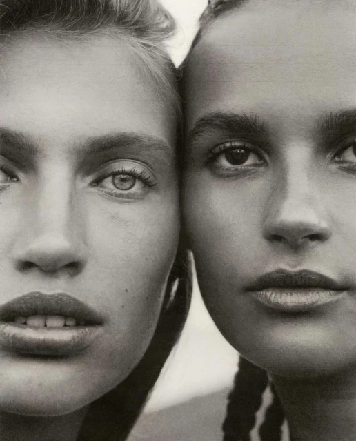 Close-up portrait of two women with contrasting skin tones and hairstyles posing together in a studio with soft, neutral lighting.