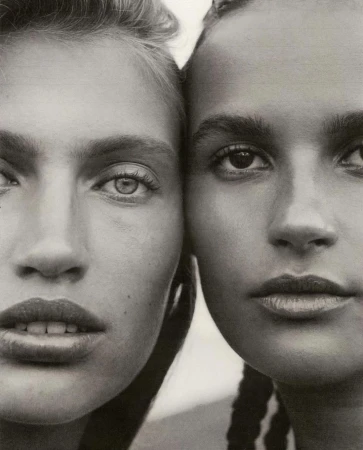 Close-up portrait of two women with contrasting skin tones and hairstyles posing together in a studio with soft, neutral lighting.
