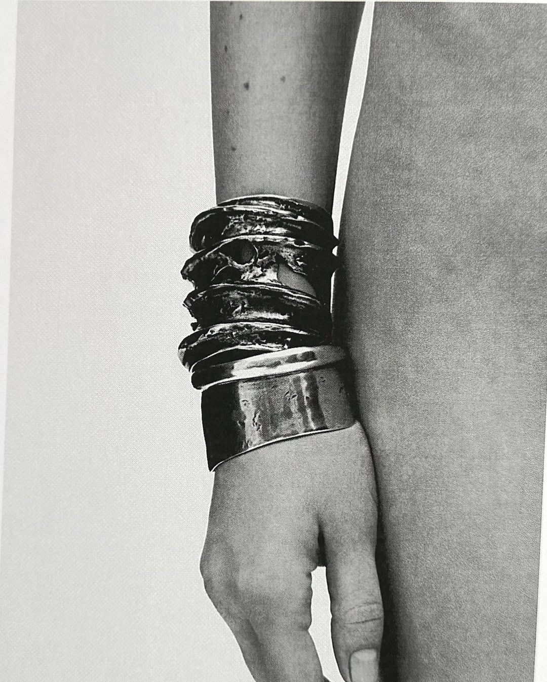 Close-up of a woman's arm adorned with a stack of silver bracelets of varying widths, creating a textured and shiny effect.