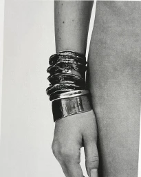 Close-up of a forearm adorned with several chunky metallic bracelets styled by Pawel Jastak in Paris.