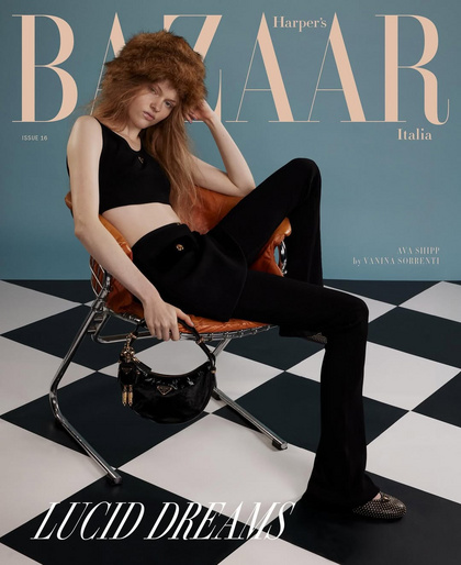 Magazine cover featuring a woman with auburn hair wearing a black crop top and pants, seated on a chair against a blue background.