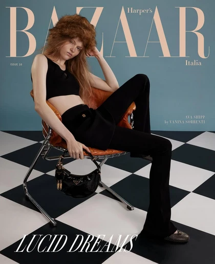 Magazine cover featuring a woman with auburn hair wearing a black crop top and pants, seated on a chair against a blue background.