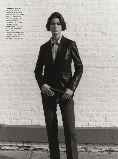 Woman in leather jacket and trousers stands against a brick wall, modeling fashion apparel and accessories for a studio shot.