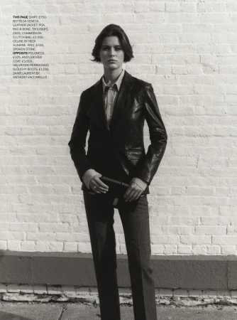 Woman in leather jacket and trousers stands against a brick wall, modeling fashion apparel and accessories for a studio shot.