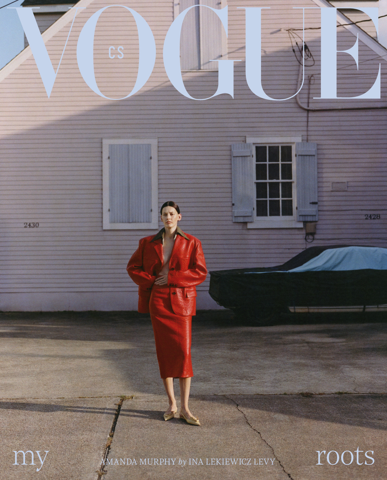 Vogue cover featuring a woman in a red suit standing on a street in front of a pink house and covered car.