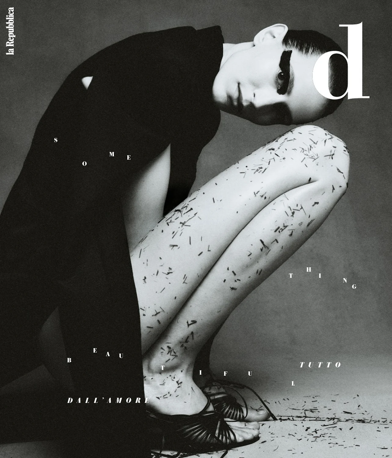 Striking black and white fashion shot of a crouching female model in a dark jacket and strappy heels, covered in abstract black elements.
