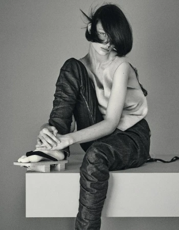 Model with dark bob hairstyle wearing dark trousers and sandals sitting on a ledge