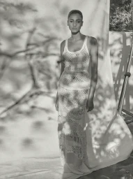 Model in a cream crocheted knit maxi dress standing in front of a white fabric backdrop outdoors.