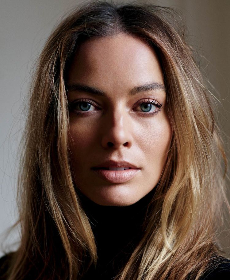 Close-up portrait of an adult woman with blond hair wearing a black turtleneck against a neutral background in a studio setting.