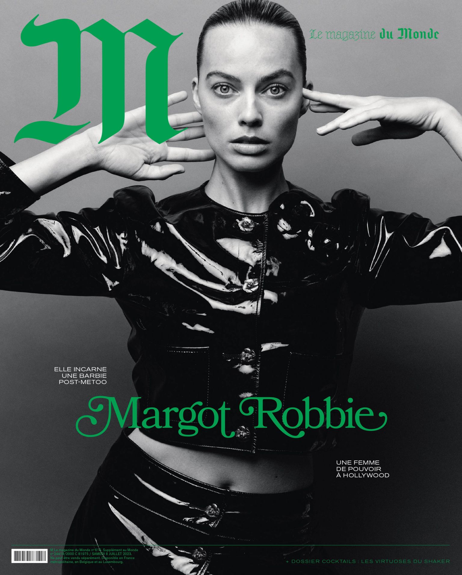 Magazine cover featuring Margot Robbie in a black glossy jacket and skirt, with large green stylized typography against a gray background.