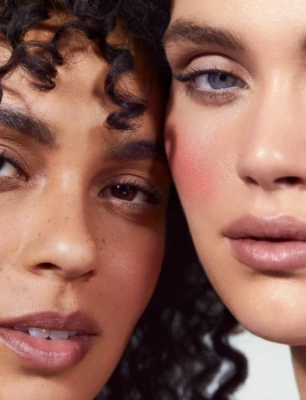Close-up portrait of two female models with detailed makeup by make-up artist Pati Dubroff against a neutral background.