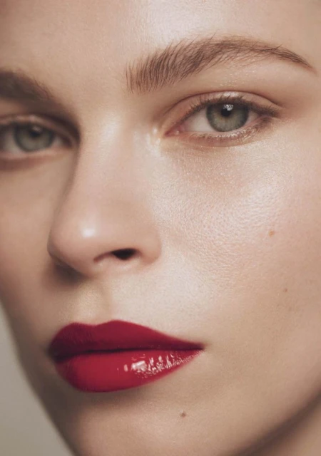 Close-up studio shot of a fair-skinned young adult woman with red lipstick, neutral expression, and light eye makeup.